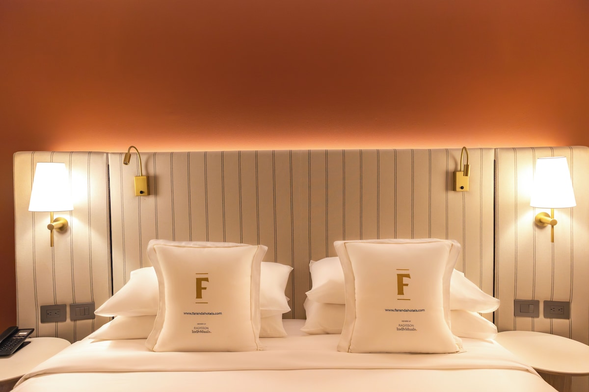 A hotel room with a large bed, two bedside lamps, and a headboard with vertical lines.