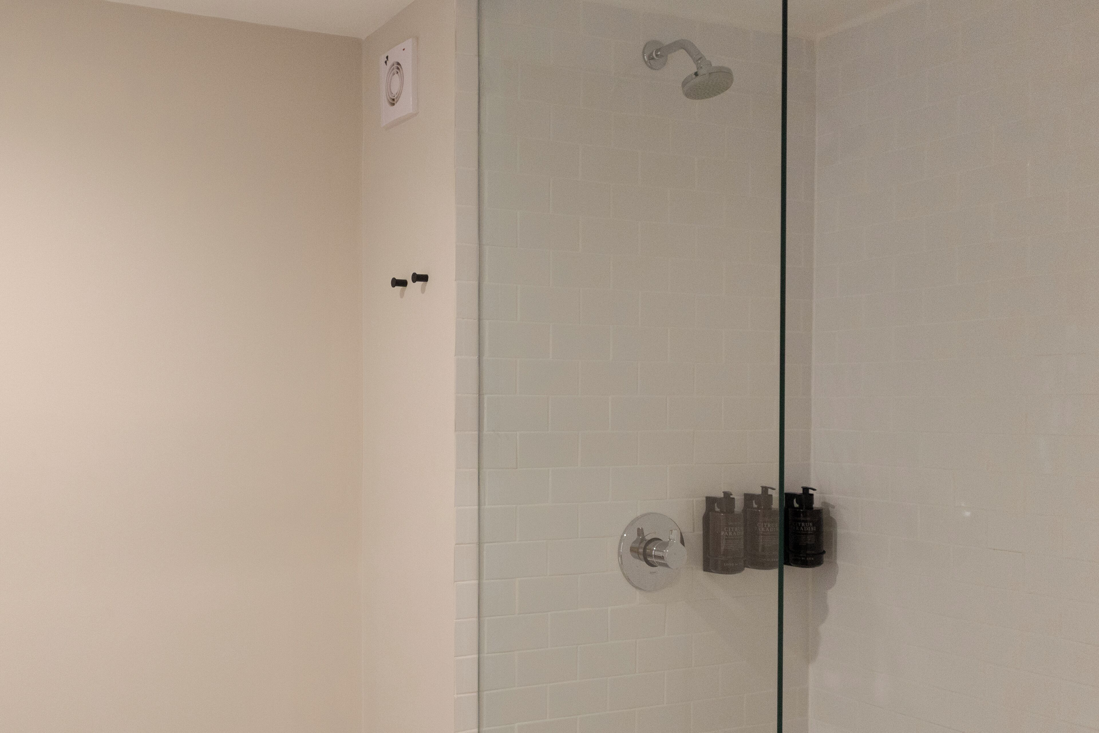 A bathroom with a glass partition, a showerhead, and a wall-mounted faucet.
