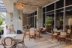 An indoor dining area with wicker chairs and tables, large windows, and a concrete ceiling. - Faranda Collection Cartagena, a member of Radisson Individuals (Cartagena)