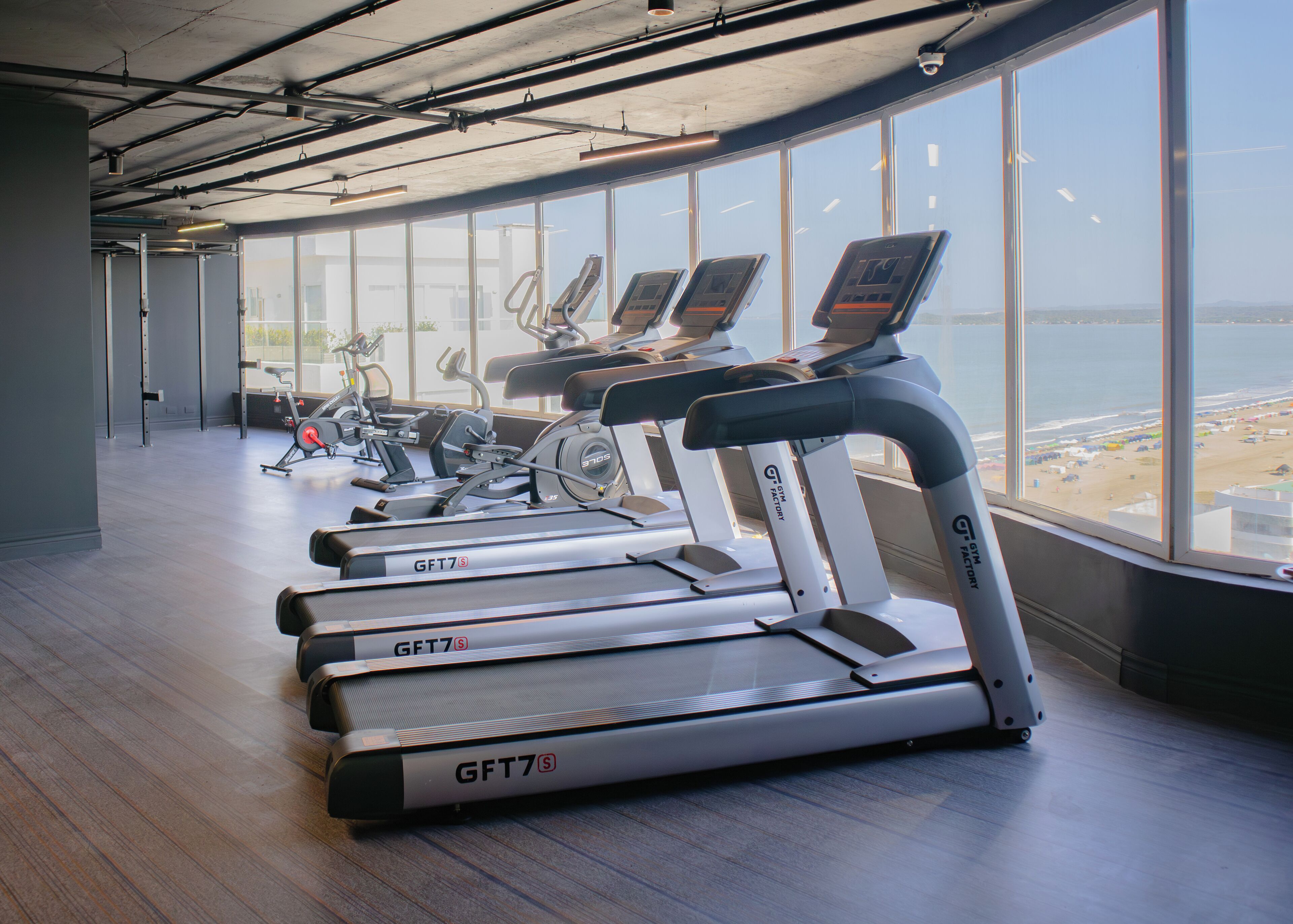 A gym with treadmills and stationary bikes, large windows with a view of the beach.