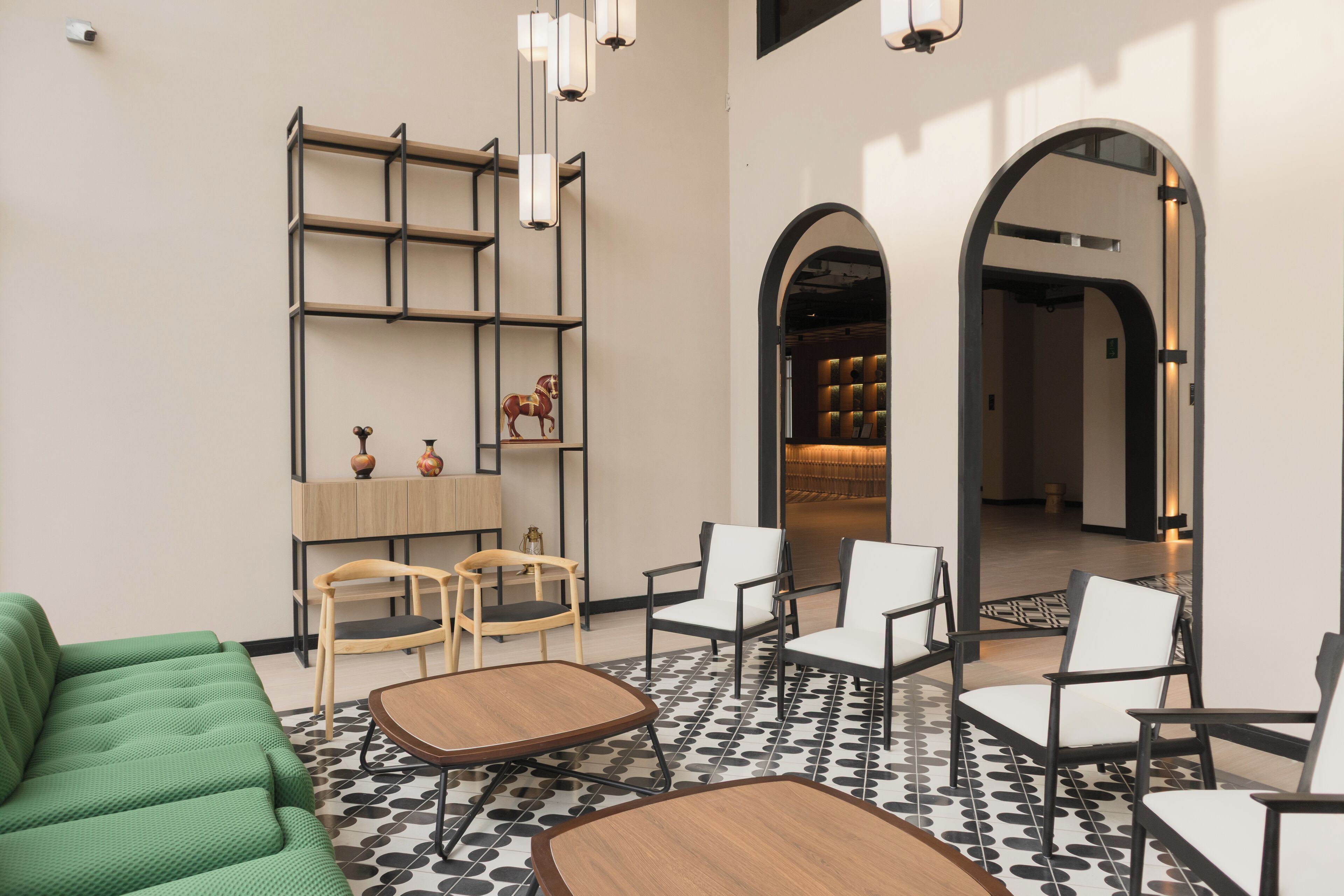 A modern interior with a green sofa, wooden coffee table, and white chairs. There are shelves with decorative items and a patterned floor.