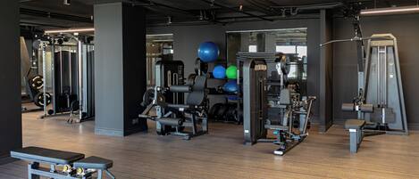 Un gimnasio con diversos equipos de ejercicio, una banca y máquinas de pesas.