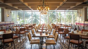 A spacious restaurant with long tables and chairs, large windows with a view of palm trees, and a central chandelier. - Faranda Collection Cartagena, a member of Radisson Individuals (Cartagena)