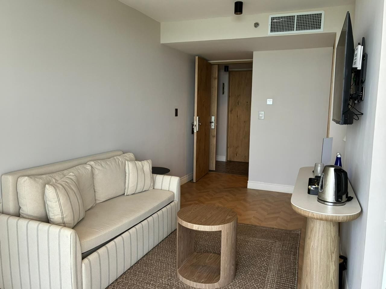 A living room with a sofa, a coffee table, a television, and a door leading to another room.