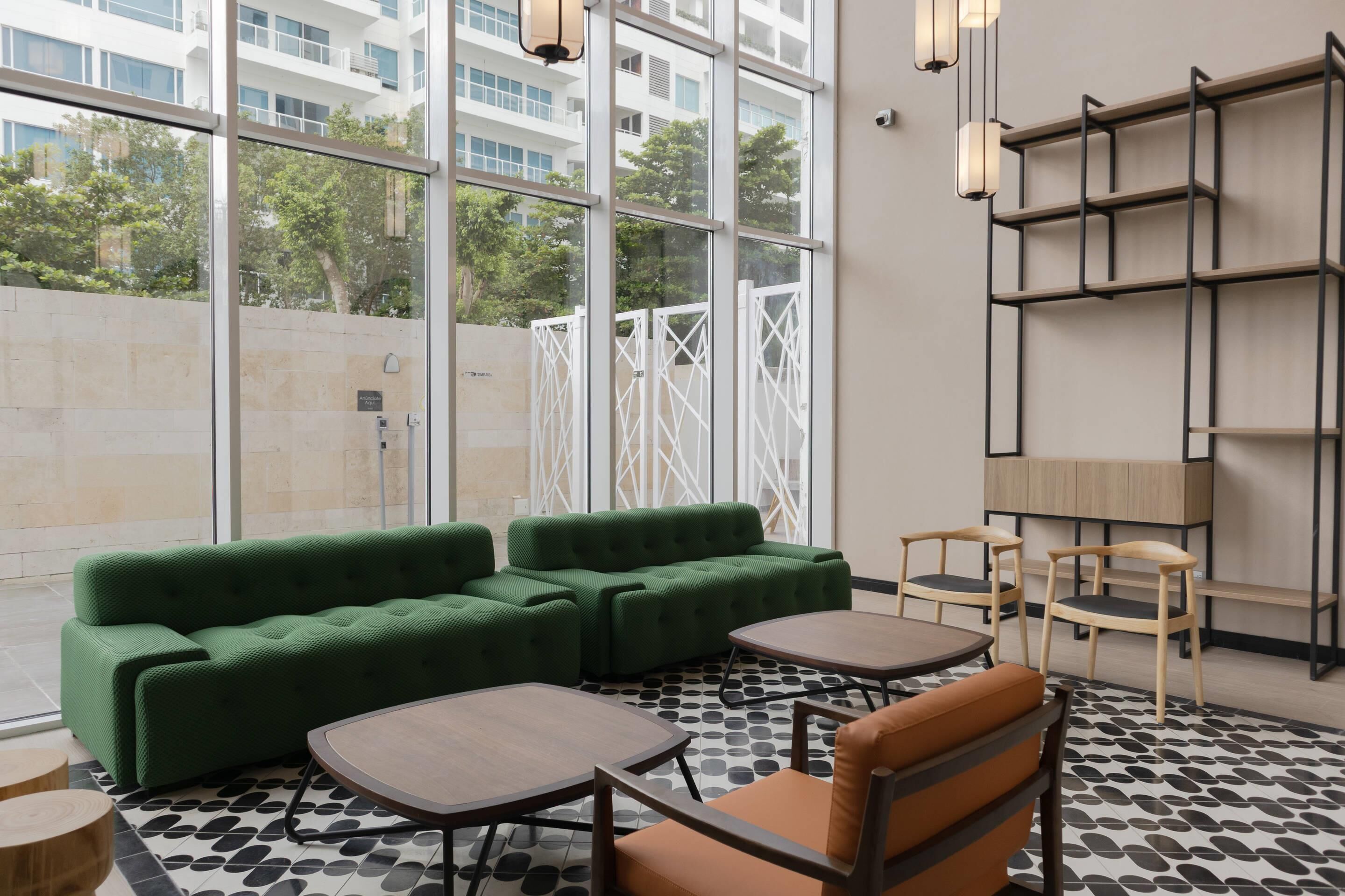 Un área de estar moderna con un sofá seccional verde, dos mesas redondas y sillas de madera.