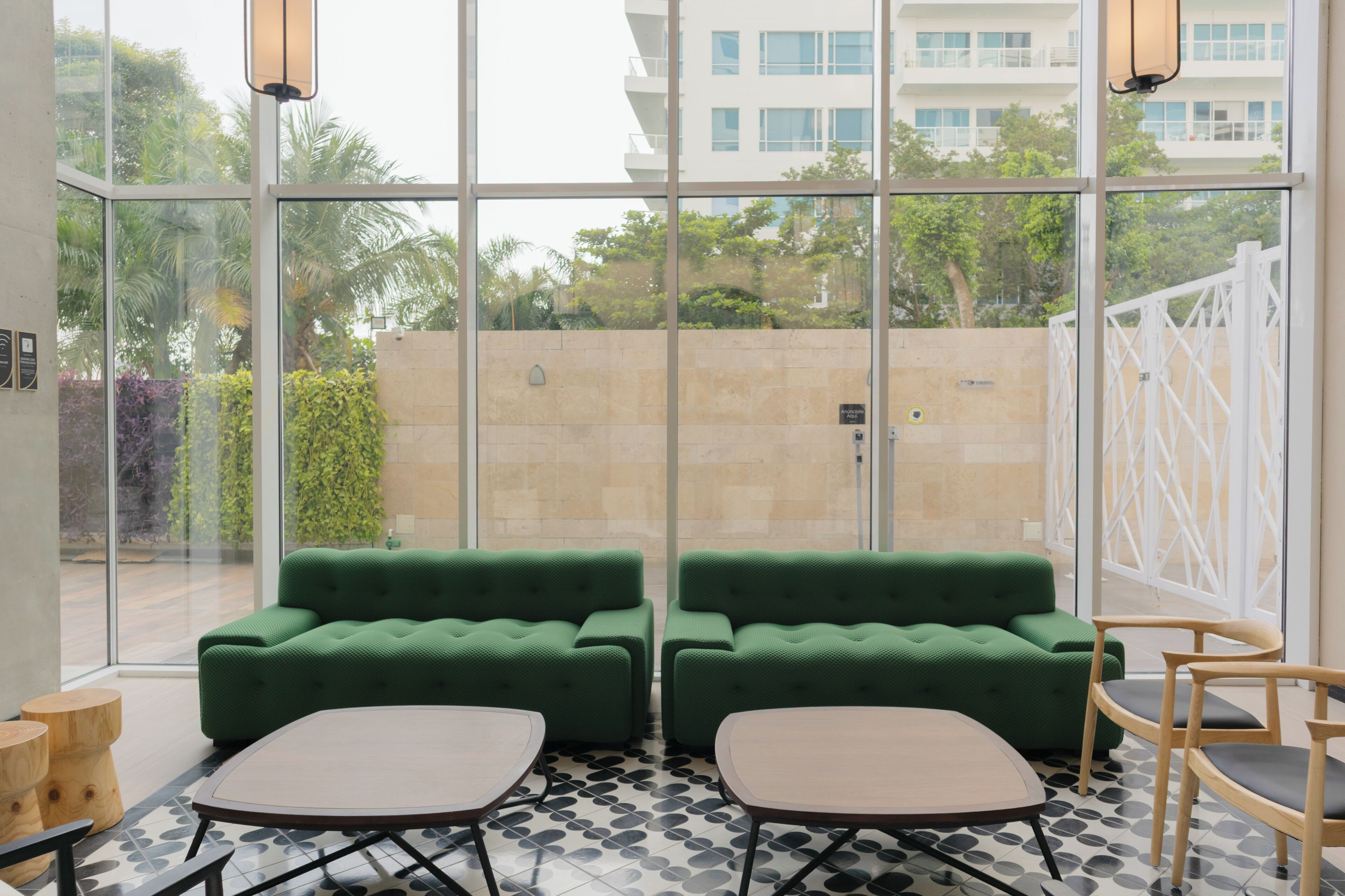 Un espace de détente intérieur moderne, avec des canapés verts et une table basse, de grandes fenêtres et un sol carrelé.
