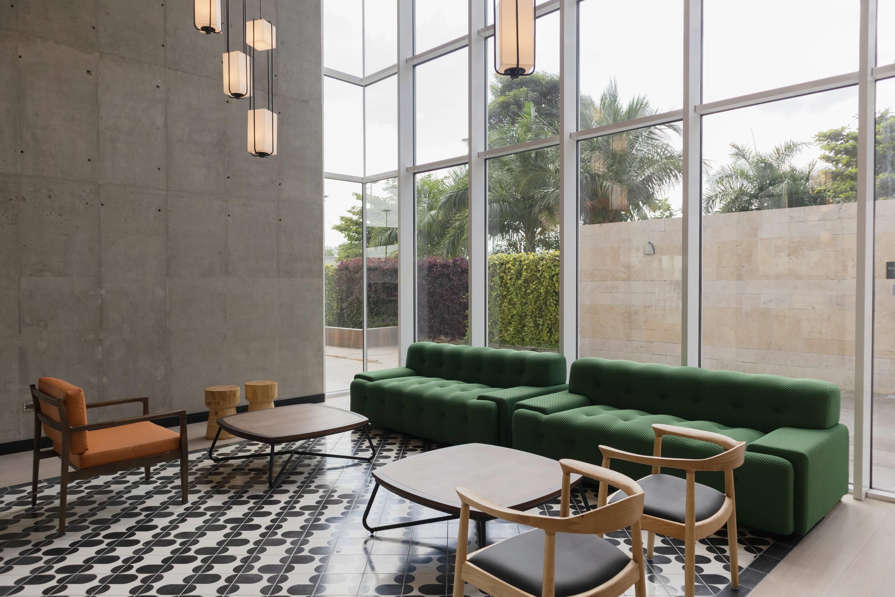 A modern indoor space with a green sofa, wooden chairs, a round table, and a patterned floor.