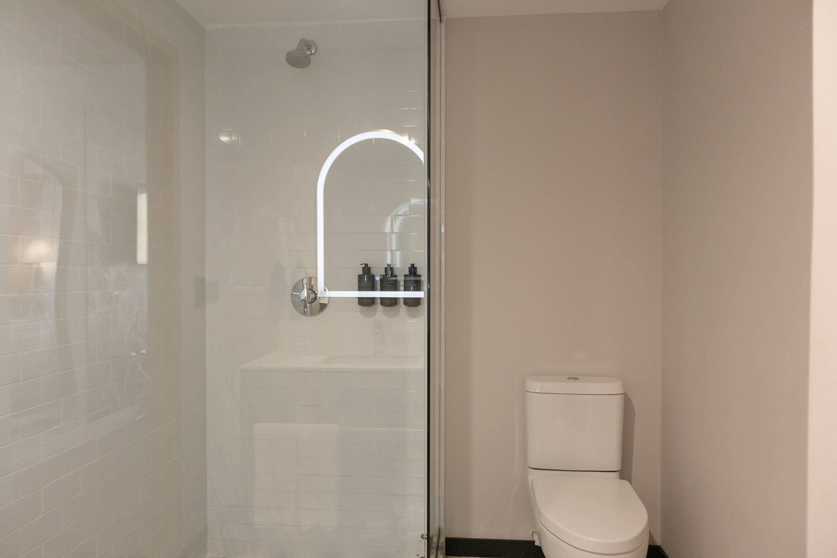 A modern bathroom with a glass shower enclosure, a white toilet, and a mirror above the sink.
