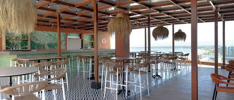 A spacious indoor area with high ceilings, wooden beams, and a patterned floor. Tables and chairs are arranged for dining, and a large window offers a view of the city skyline.