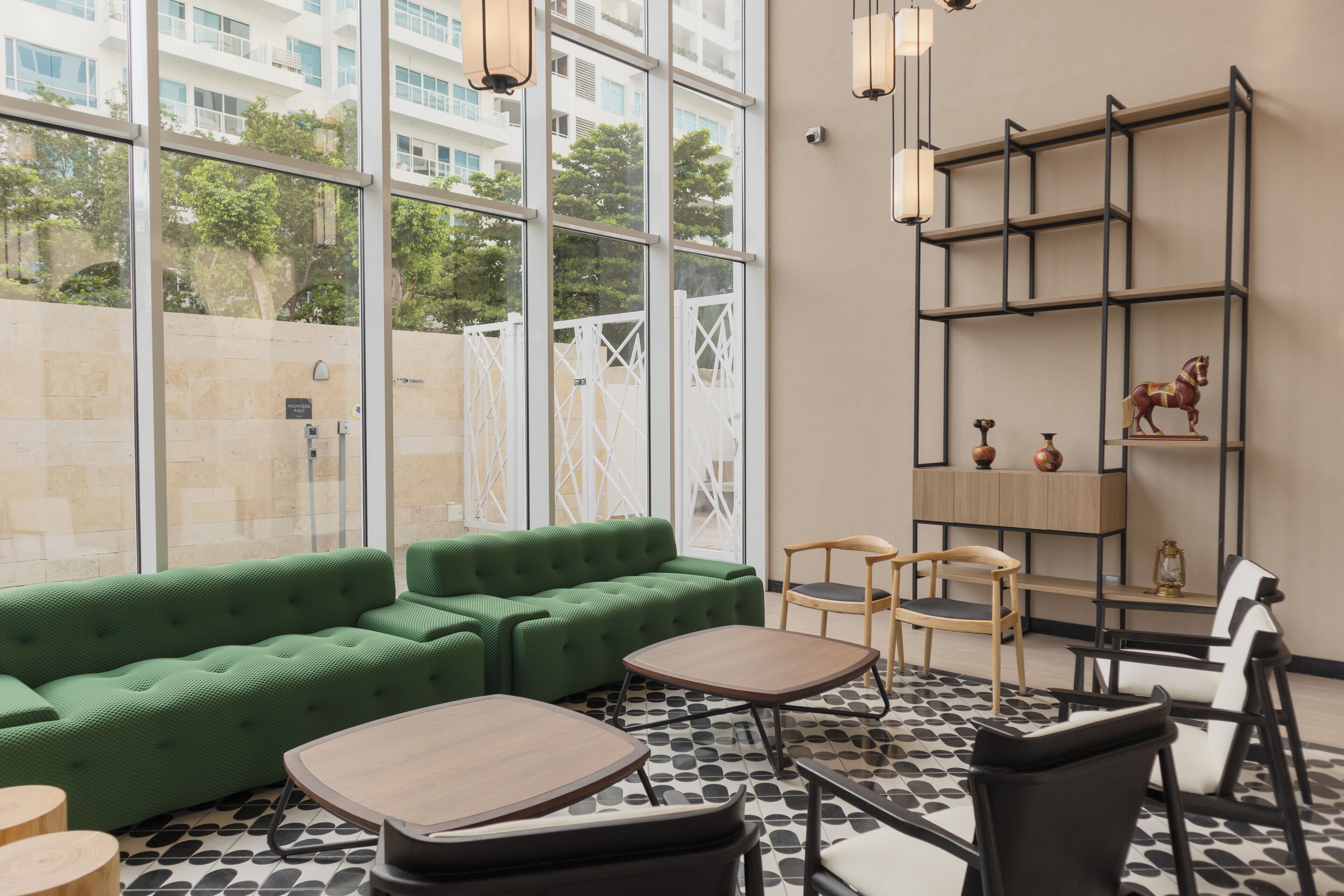 A modern lounge area with a green sofa, wooden tables, and a black and white patterned floor.