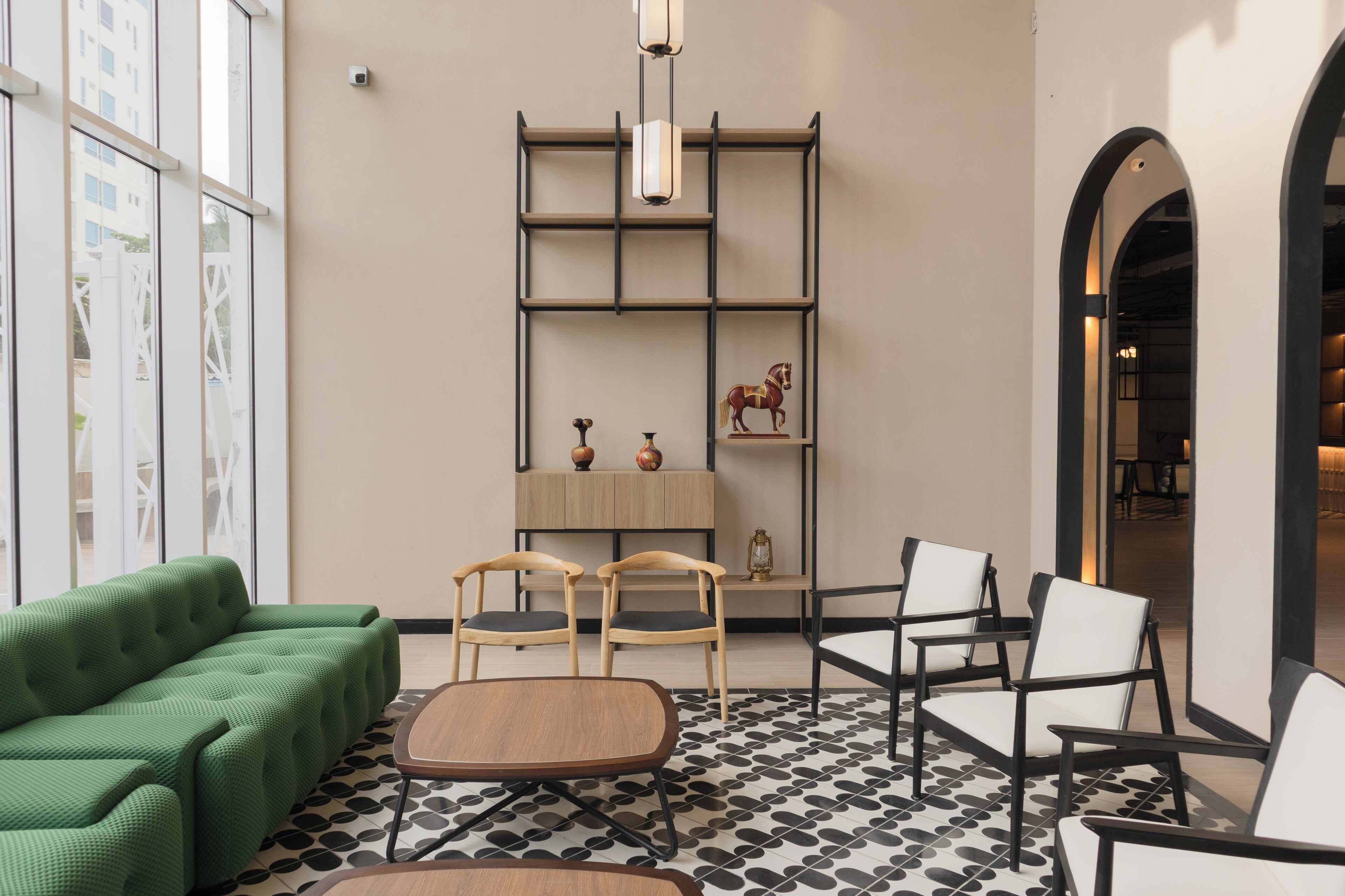 A modern interior with a green sofa, wooden chairs, a patterned floor, and a bookshelf with decorative items.
