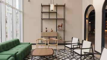 A modern interior with a green sofa, wooden chairs, a patterned floor, and a bookshelf with decorative items.