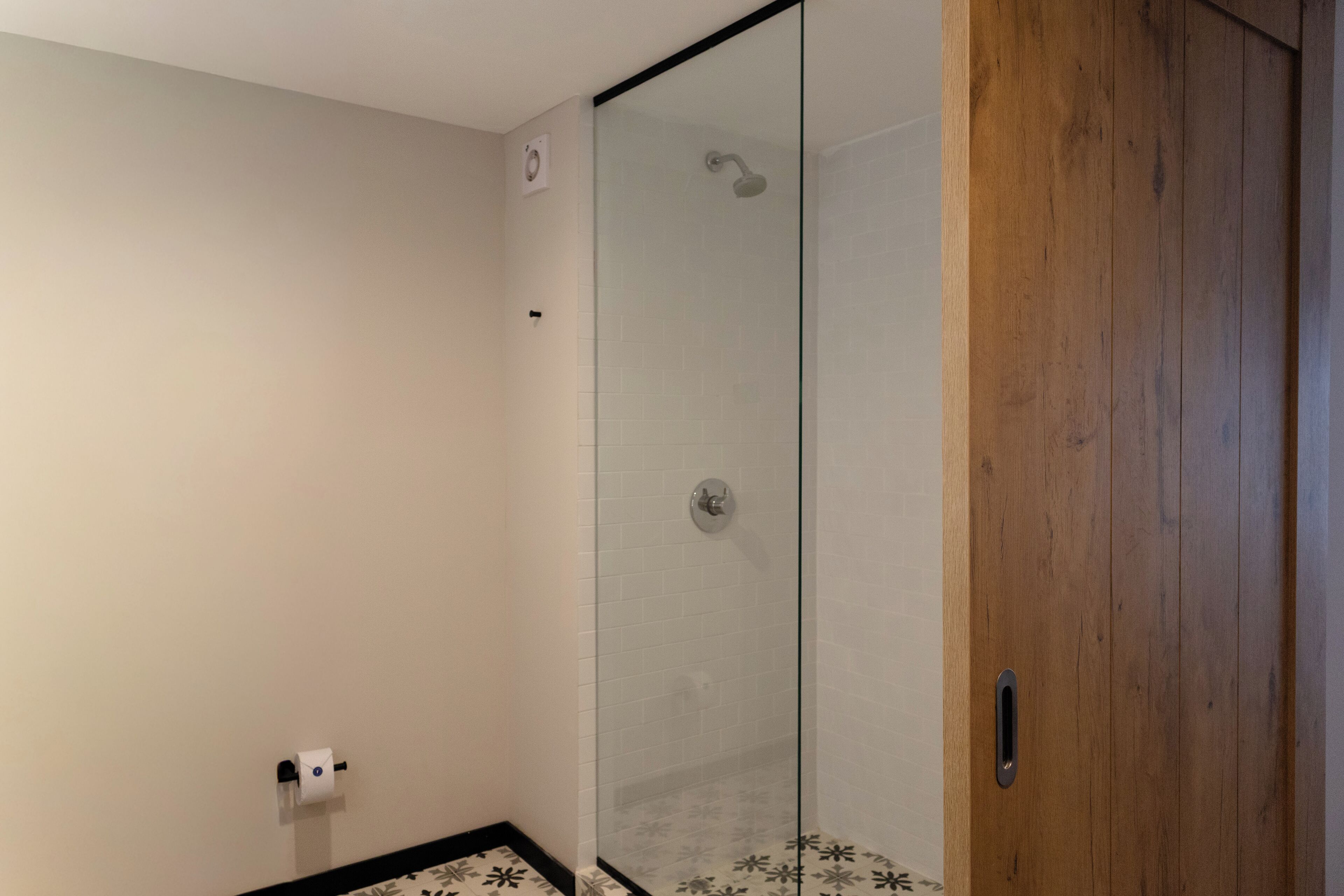 A bathroom with a glass shower enclosure, a wooden door, and a toilet paper holder on the wall.