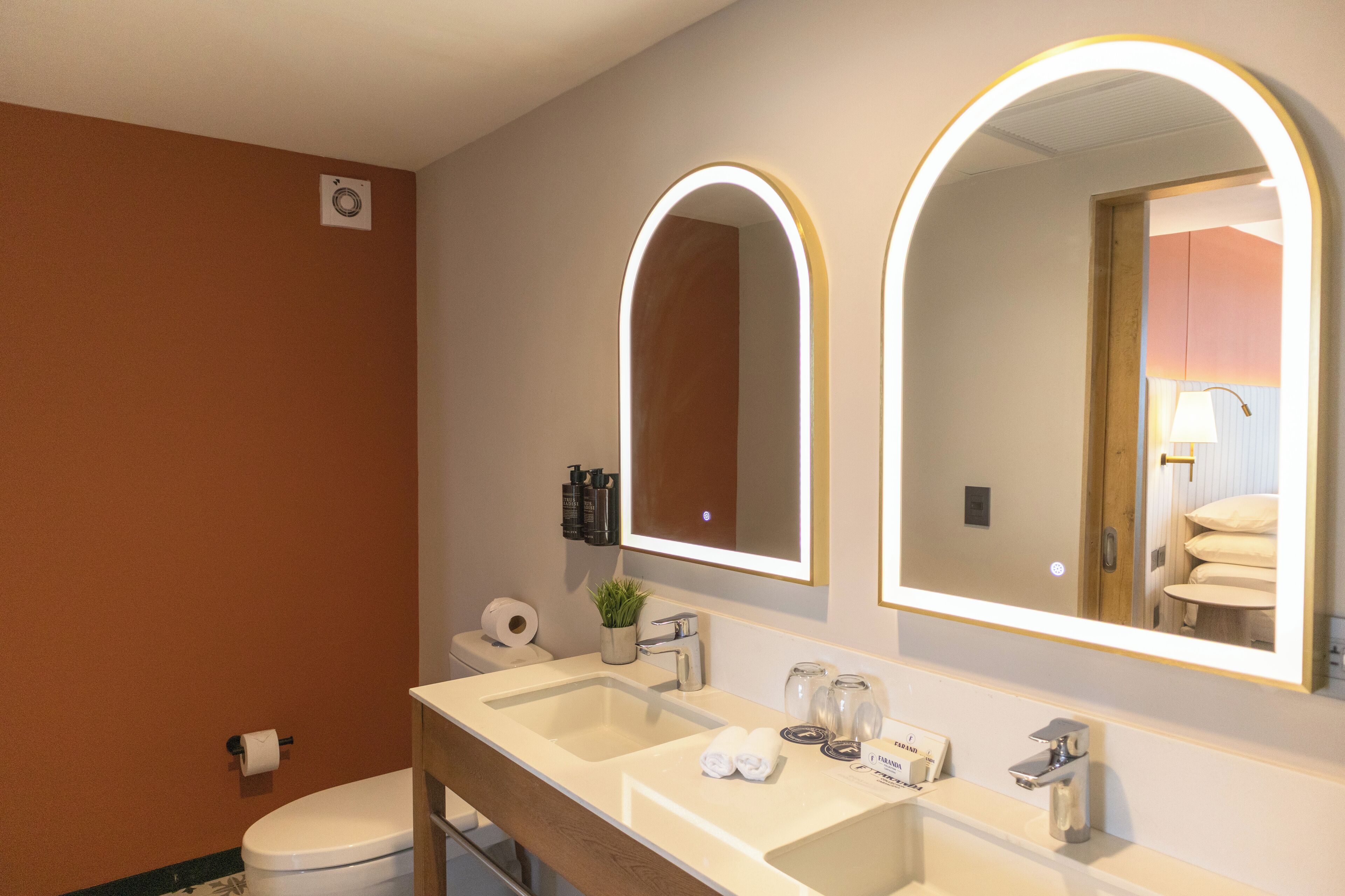 A modern bathroom with a double sink, a toilet, and two large mirrors with illuminated frames.