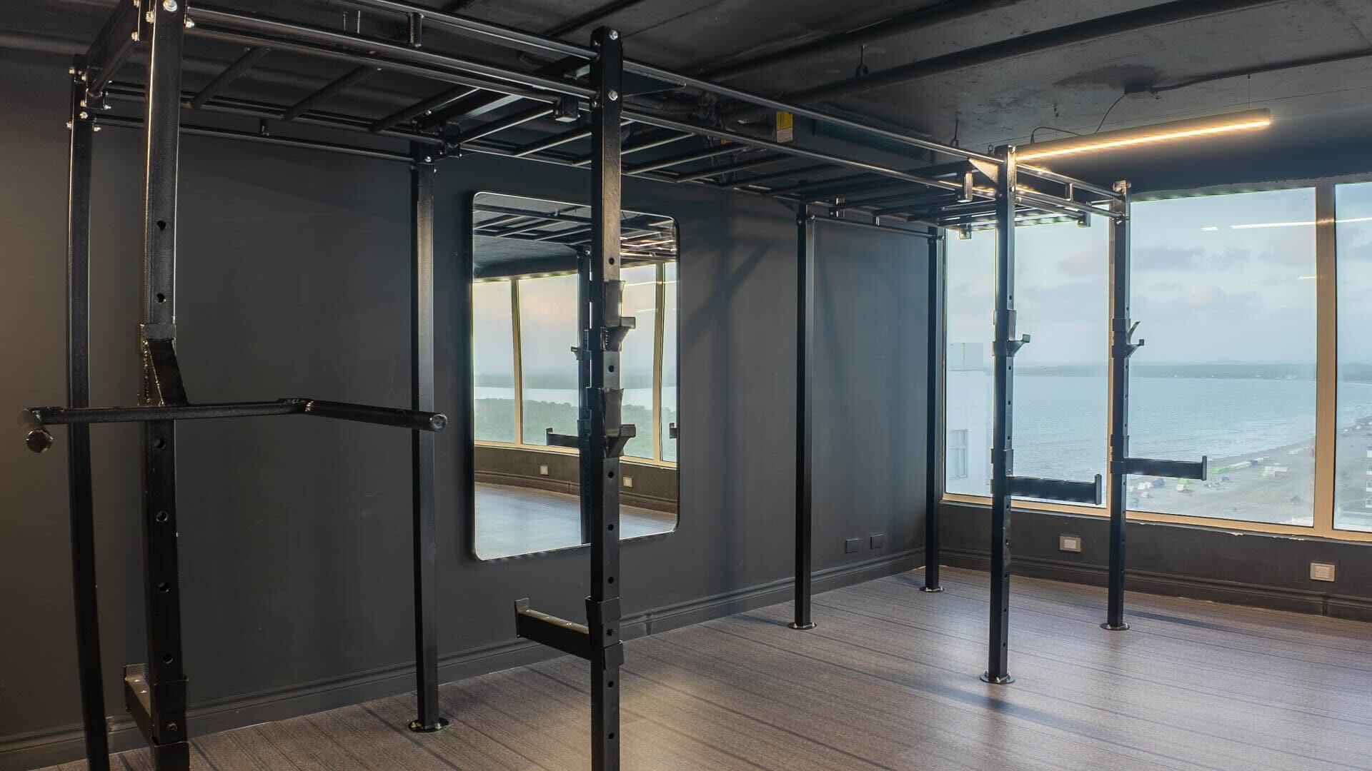 A gym with a pull-up bar system, large windows with a view of the sea, and a wooden floor.