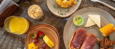 Een ontbijttafel met borden vol roerei, toast en fruit, waaronder druiven en ananas.