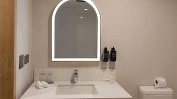 A modern bathroom with a white sink, a mirror with an arch top, and toiletries on the wall.