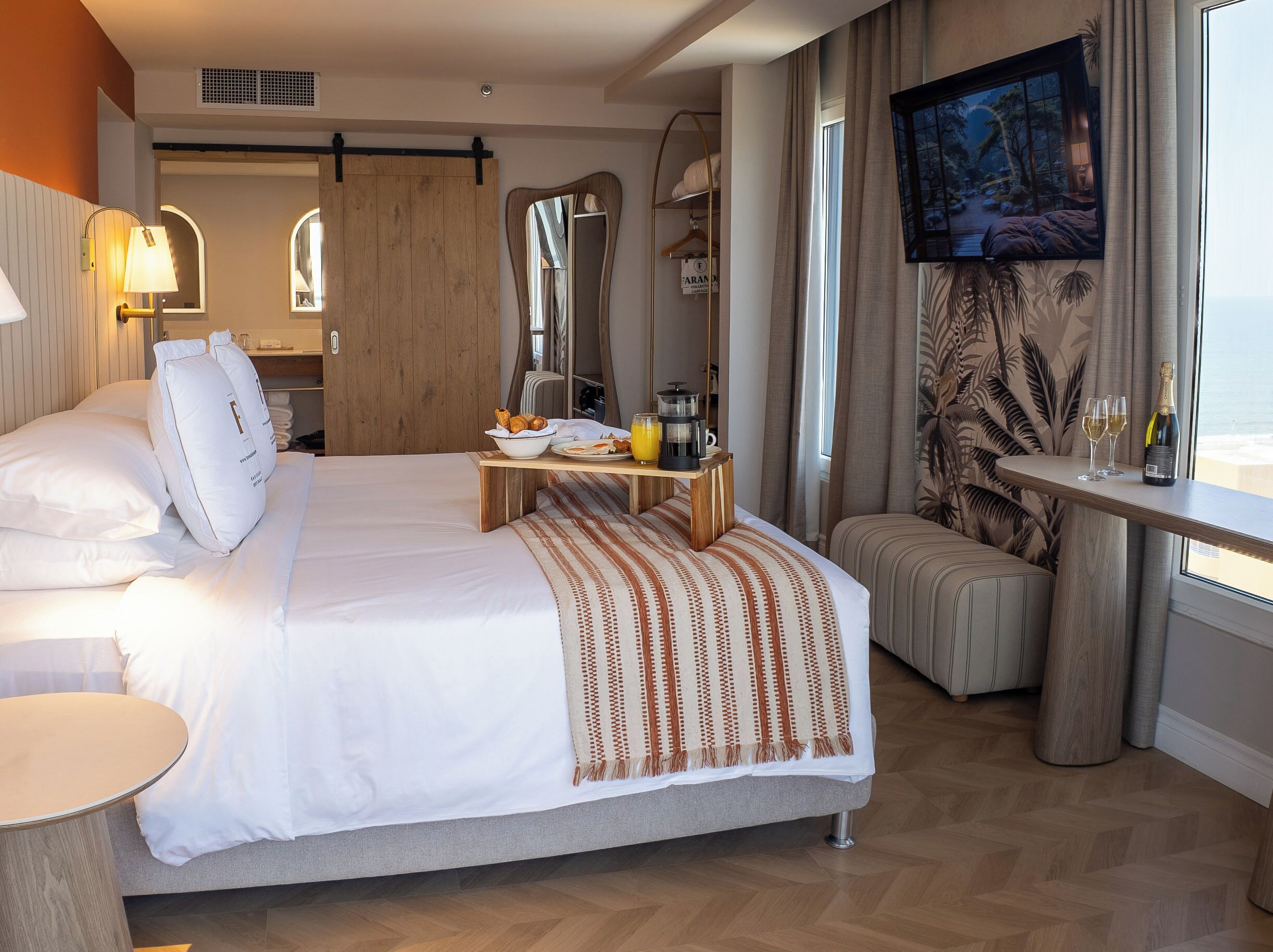 A hotel room with a bed, bedside table, TV, and a view of the outdoors.