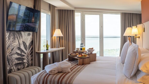 A hotel room with a large bed, a seating area with a table, a TV, and a view of the outdoors. - Faranda Collection Cartagena, a member of Radisson Individuals (Cartagena)