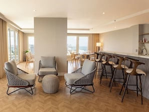 A modern living room with a bar area, large windows, and a view of the cityscape.