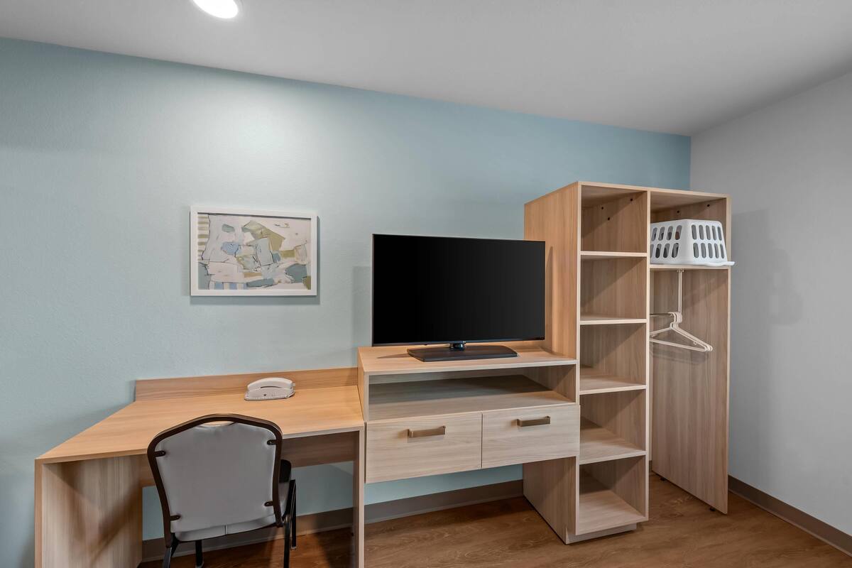 A room with a wooden desk, a chair, a television, a wardrobe, and a map on the wall.