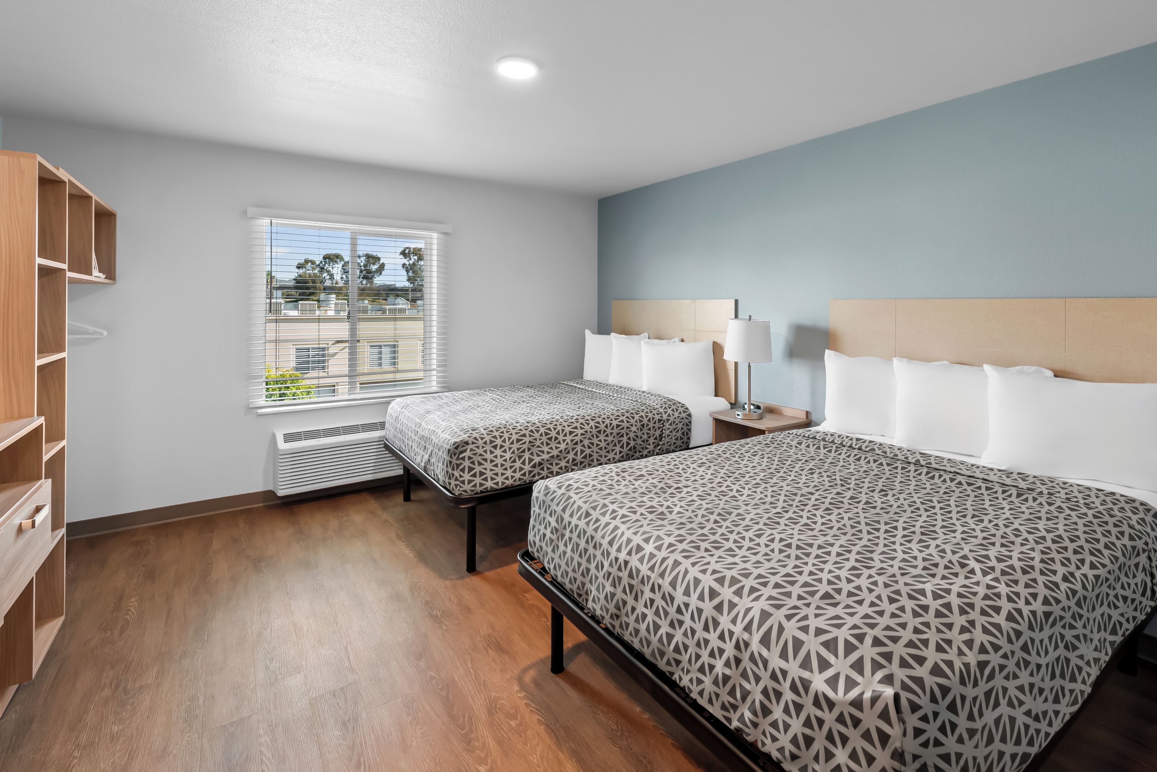 A hotel room with two beds, a window with blinds, a heater, and a wooden wardrobe.