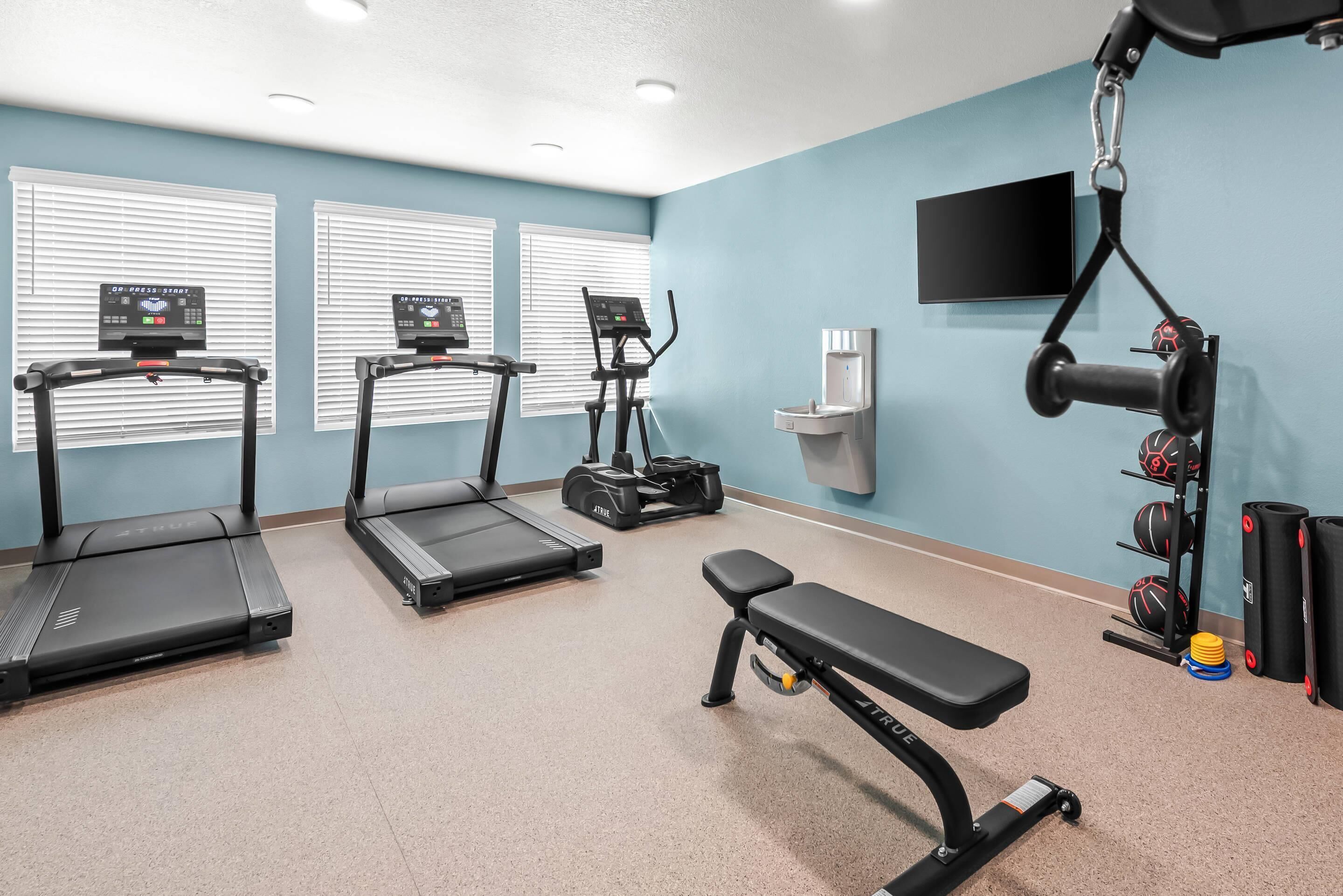 A gym with treadmills, an elliptical, a bench, and a wall-mounted TV.