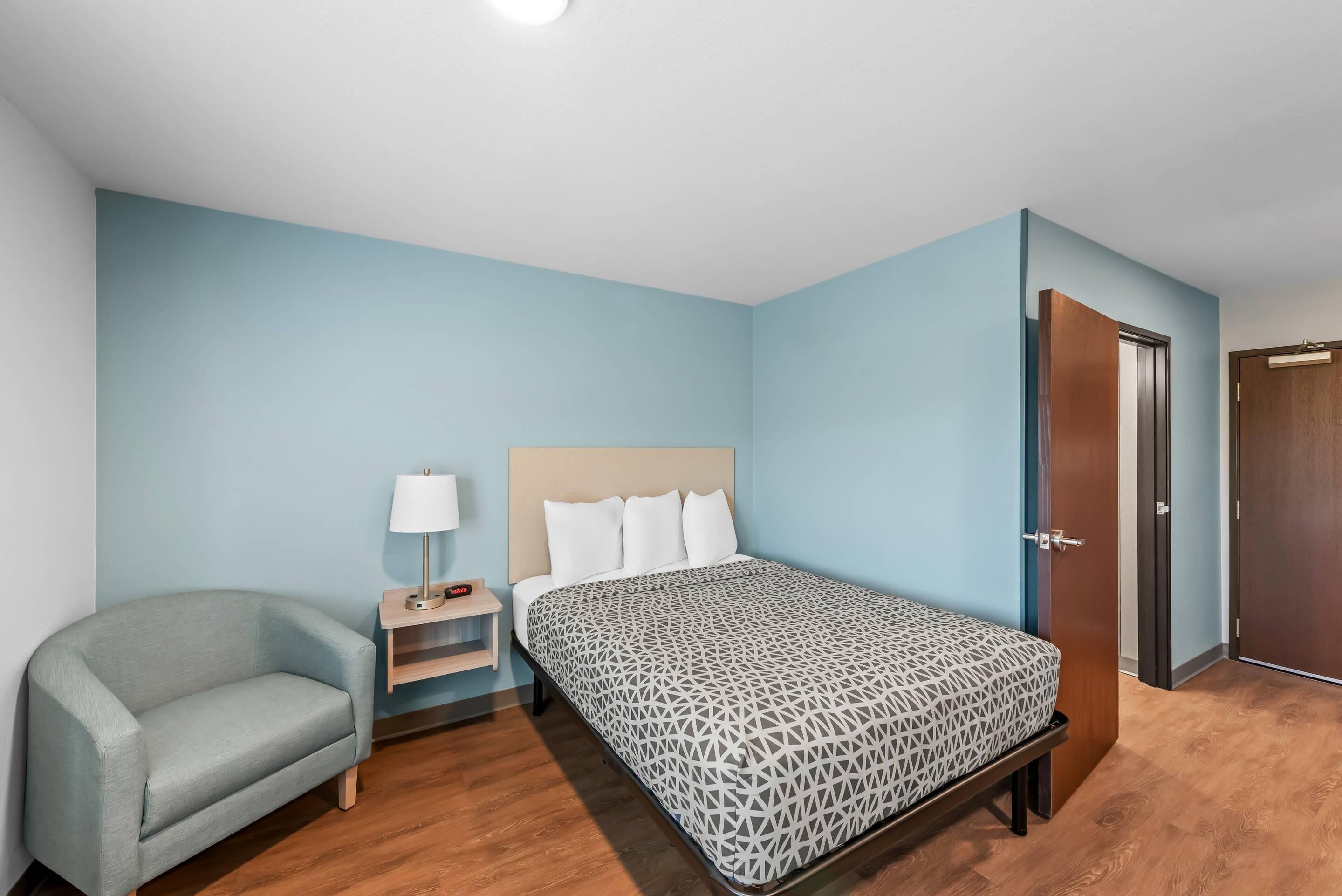 A bedroom with a bed, a chair, a nightstand, and a door.