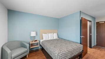 A bedroom with a bed, a chair, a nightstand, and a door.