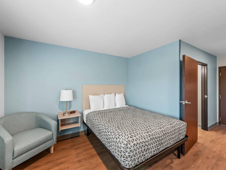 Ein Schlafzimmer mit einem Bett, einem Sessel, einem Nachttisch und einer Tür.