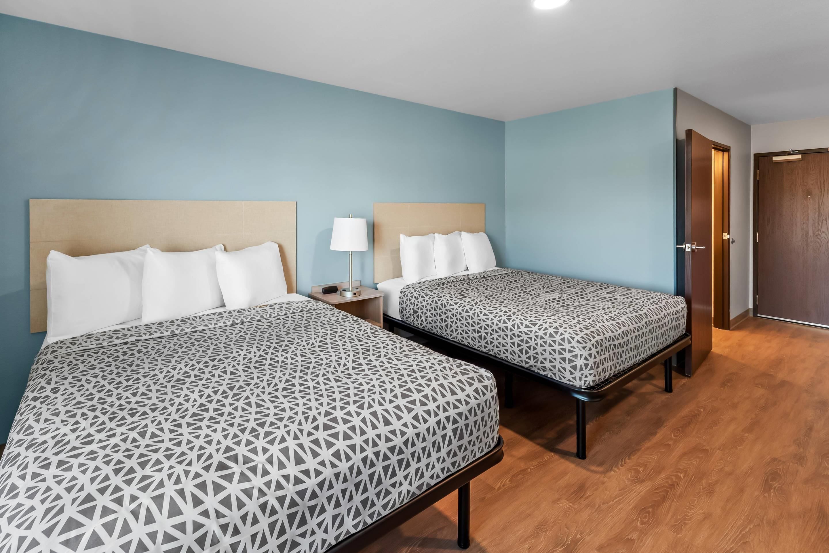 A hotel room with two beds, a nightstand, a lamp, and a wooden door.