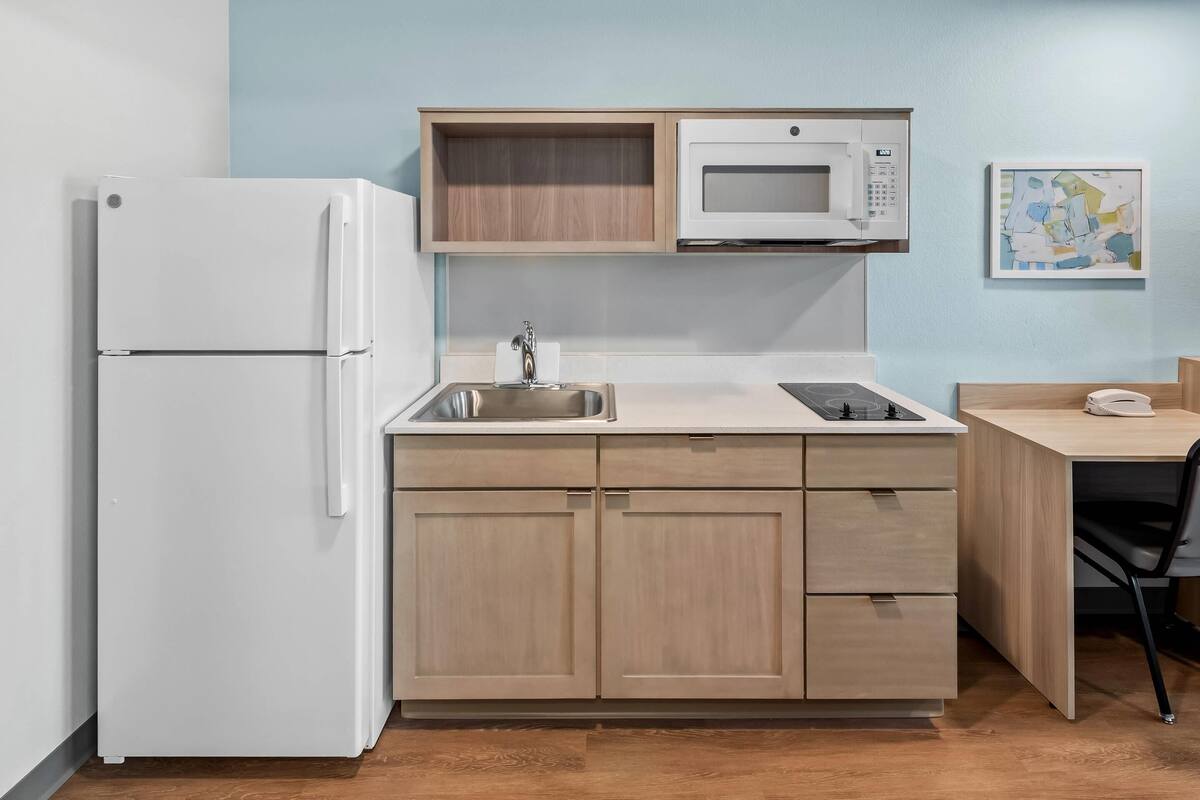 A compact kitchenette with a refrigerator, microwave, sink, and wooden cabinets.