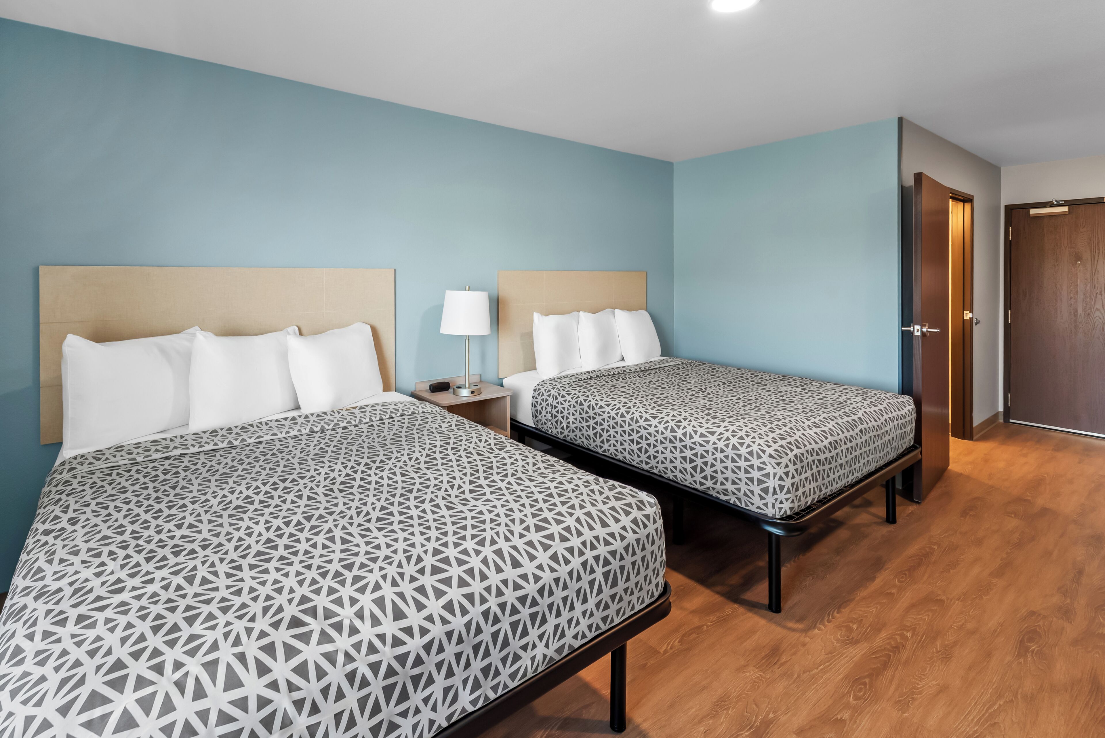A hotel room with two beds, a nightstand with a lamp, and a wooden door.