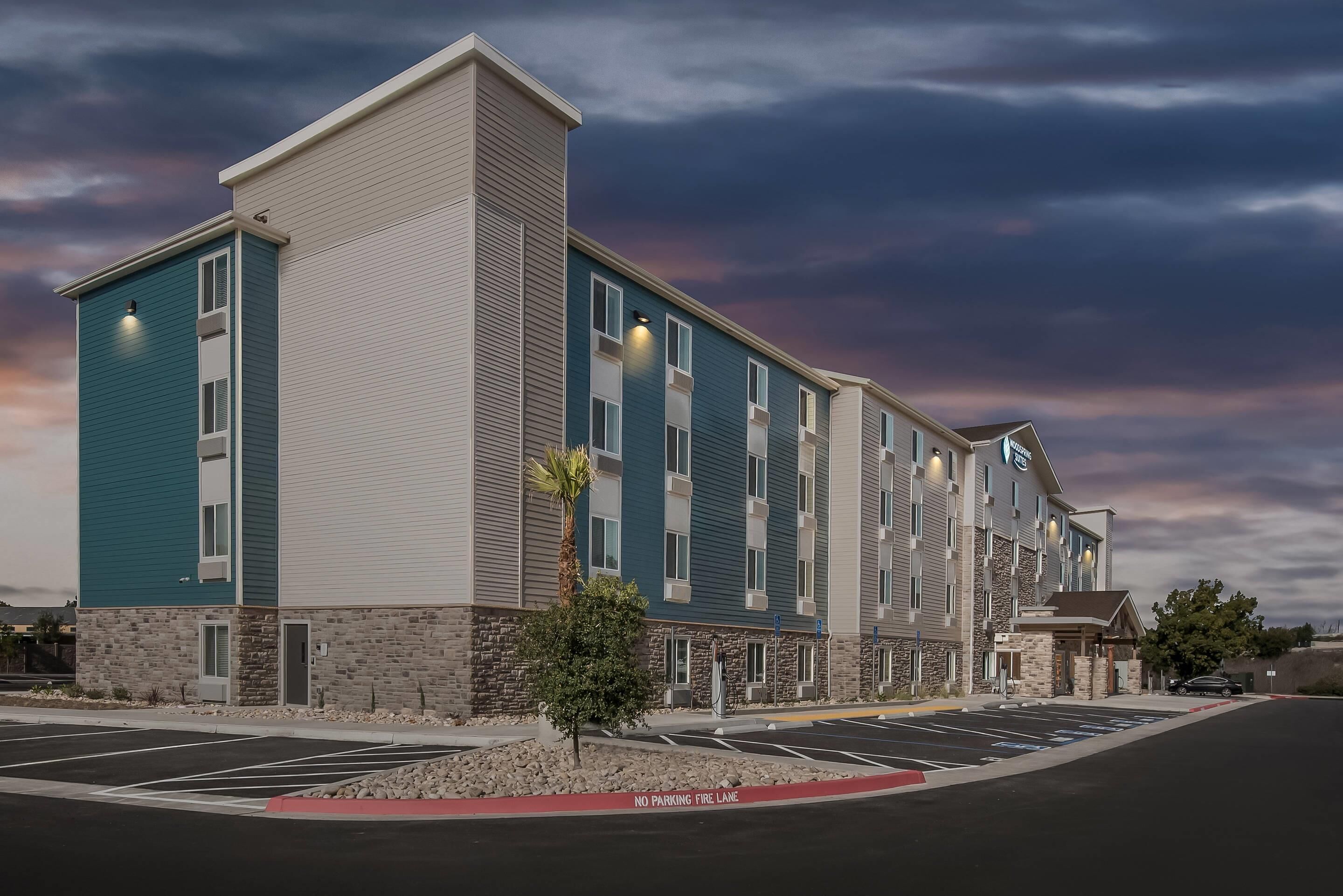 A multi-story hotel with a modern design, featuring a mix of stone and siding exteriors, and a parking lot with marked spaces.