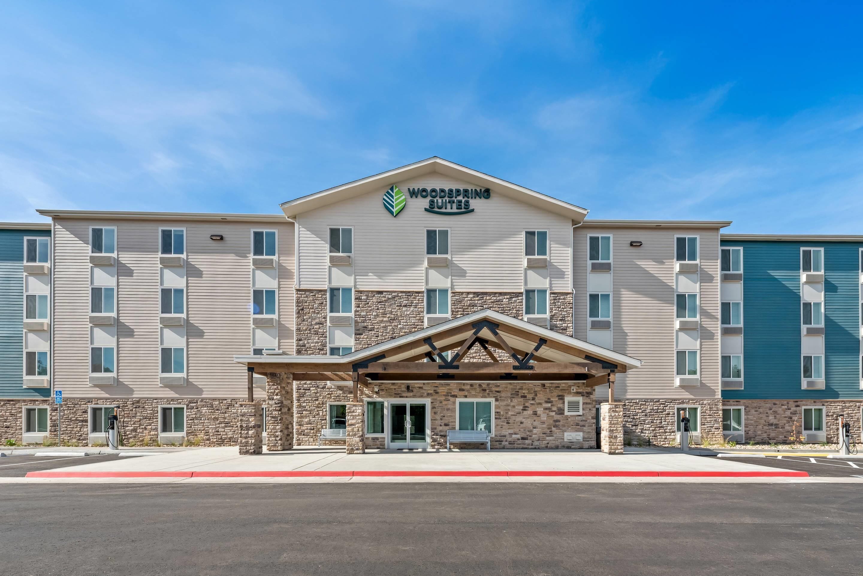 A multi-story hotel with a prominent "Woodspring Suites" sign, a covered entrance, and a stone facade.