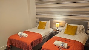 Une chambre d’hôtel avec deux lits, chacun recouvert d’une couverture rouge et agrémenté d’oreillers blancs, un mur à rayures et un luminaire suspendu rouge.