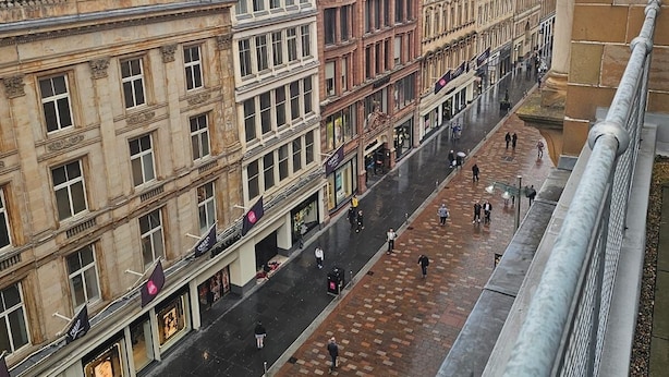 Une vue de rue avec des bâtiments historiques, une large zone piétonne et une structure moderne dotée d’une façade en verre.