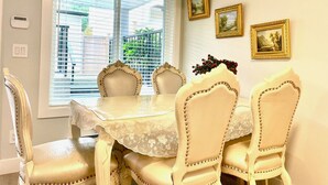 A dining area with a table and chairs, a window with blinds, and three framed pictures on the wall. - Brand New Haven (Surrey)