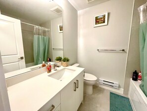 A modern bathroom with a white sink, mirror, and toilet. There are two potted plants on the counter, a towel rack on the wall, and a shower curtain. - Brand New Haven (Surrey)