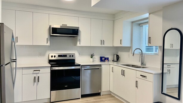 A modern kitchen with white cabinets, stainless steel appliances, and a wooden floor. - Brand New Haven (Surrey)