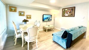 A living room with a dining table, white chairs, a blue sofa, a TV, and framed pictures on the walls. - Brand New Haven (Surrey)