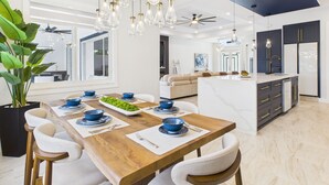 Una cocina moderna con una isla central, iluminación colgante y un comedor con mesa y sillas de madera.