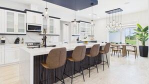 Una cocina moderna con armarios blancos, una isla central con taburetes de bar y un comedor con un gran ventanal.
