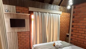 A bedroom with a wooden ceiling, a TV mounted on the wall, a bed with white bedding, and curtains. - POUSADA DECK PEREIRÃO (Santa Terezinha)