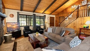 A cozy living room with a wooden ceiling, a fireplace, a television, and a staircase.