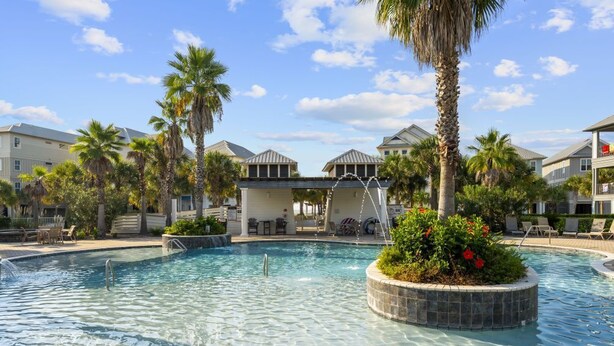 A swimming pool with a circular island, palm trees, and a covered area with seating. - Southern Exposure | Balcony (Orange Beach)