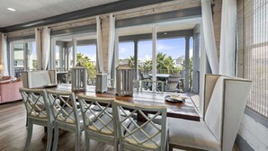 A spacious outdoor dining area with a wooden table and chairs, large windows, and a view of palm trees and buildings. - Southern Exposure | Balcony (Orange Beach)
