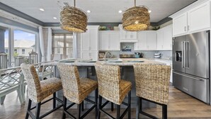 A modern kitchen with white cabinets, a stainless steel refrigerator, and a central island with bar stools. - Southern Exposure | Balcony (Orange Beach)