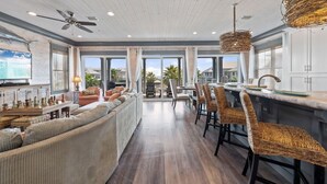 A spacious living area with a sofa, chairs, a dining table, and a kitchen area with bar stools. - Southern Exposure | Balcony (Orange Beach)