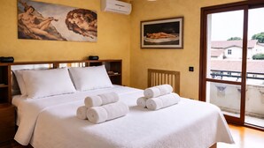 A hotel room with a bed, pillows, rolled towels, a painting, a framed picture, and a view through a window. - Whole house in Magenta | Business, families, Milan/Rho (Magenta)